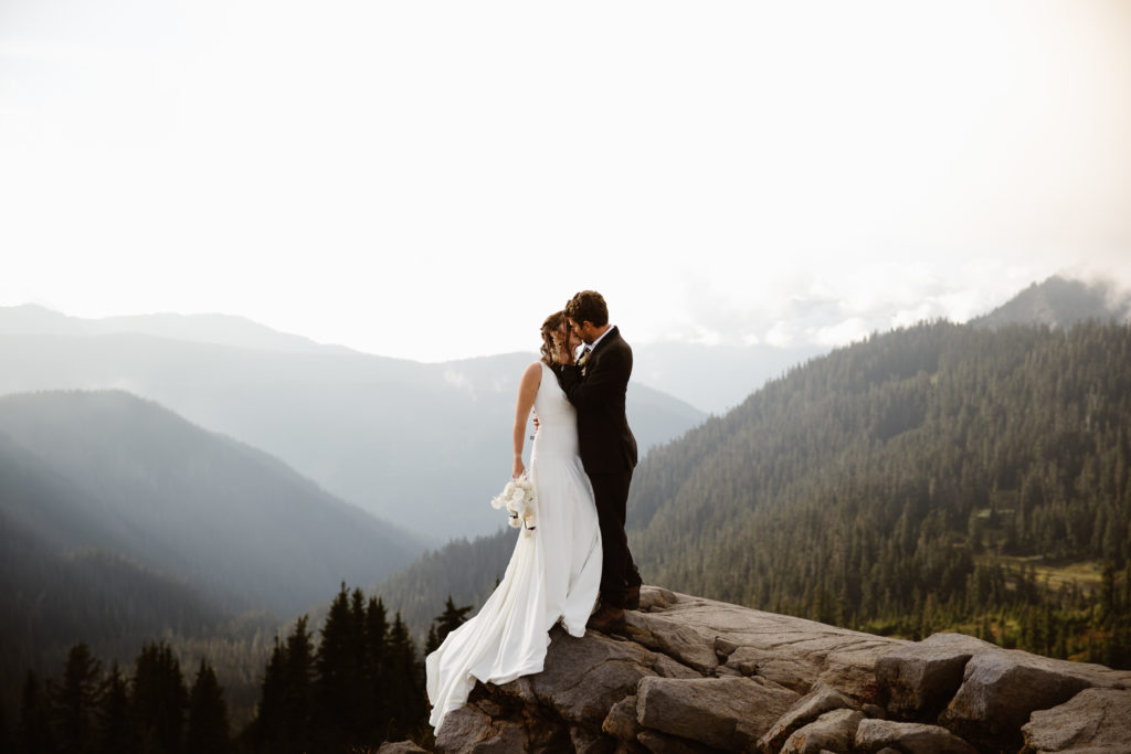 a bride and groom kiss while standing on a rock above a cliff during their north cascades elopement