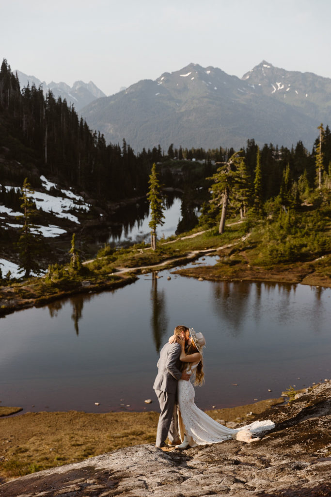 a bride and groom have their first kiss in front of an alpine lake during their north cascades elopement