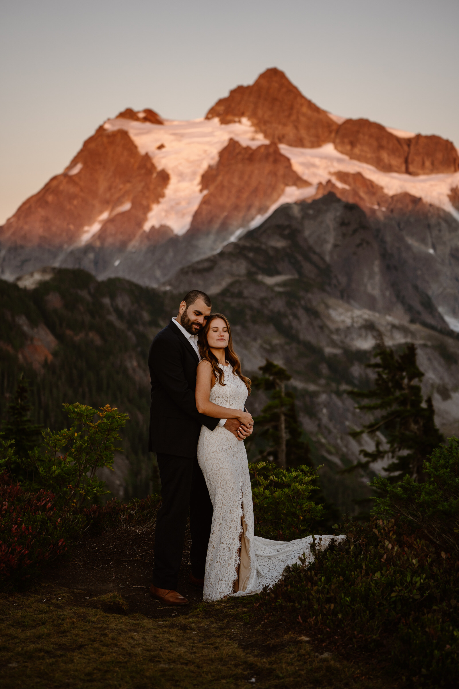 a bride hugs a groom from behind as they stand on a rock above a cliff during their north cascades elopement
