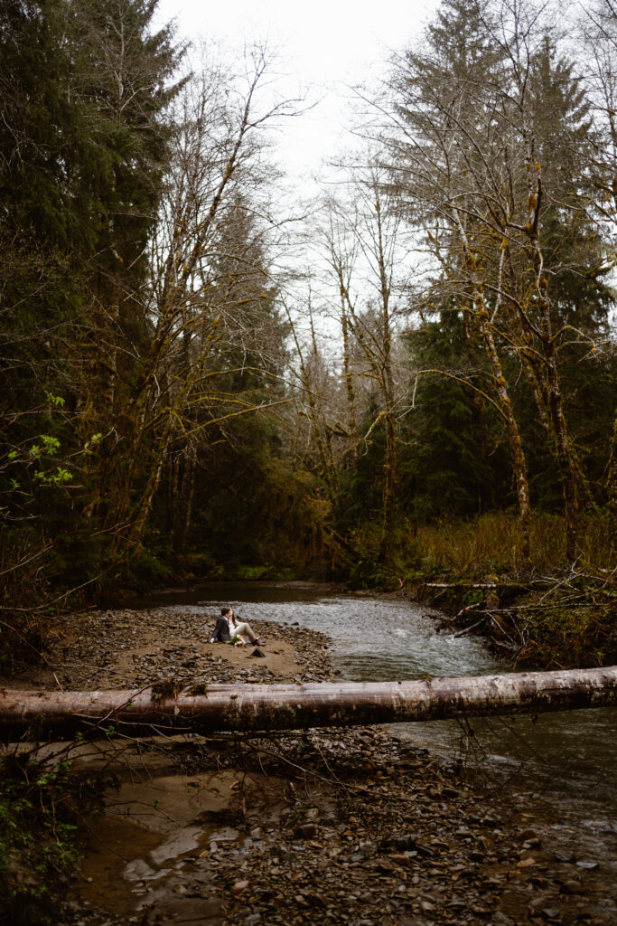 a bride and groom sit by the river during their olympic peninsula elopement