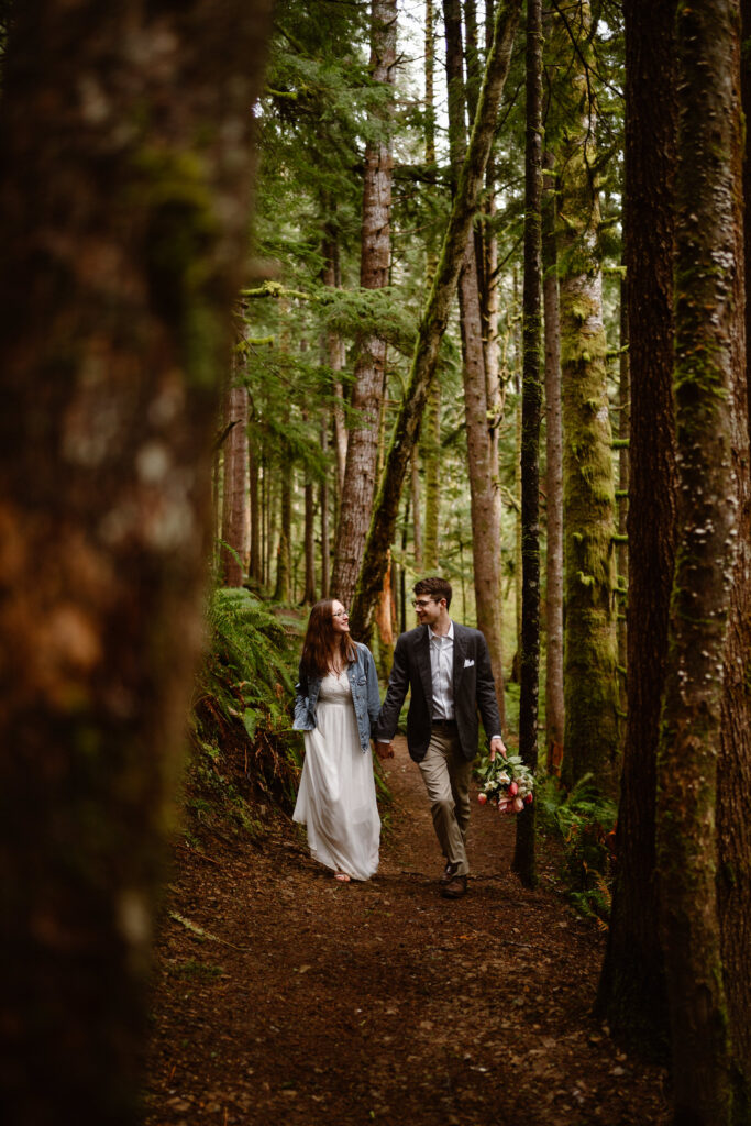 a bride and groom hold hands and explore the forests of the olympic peninsula during their elopement