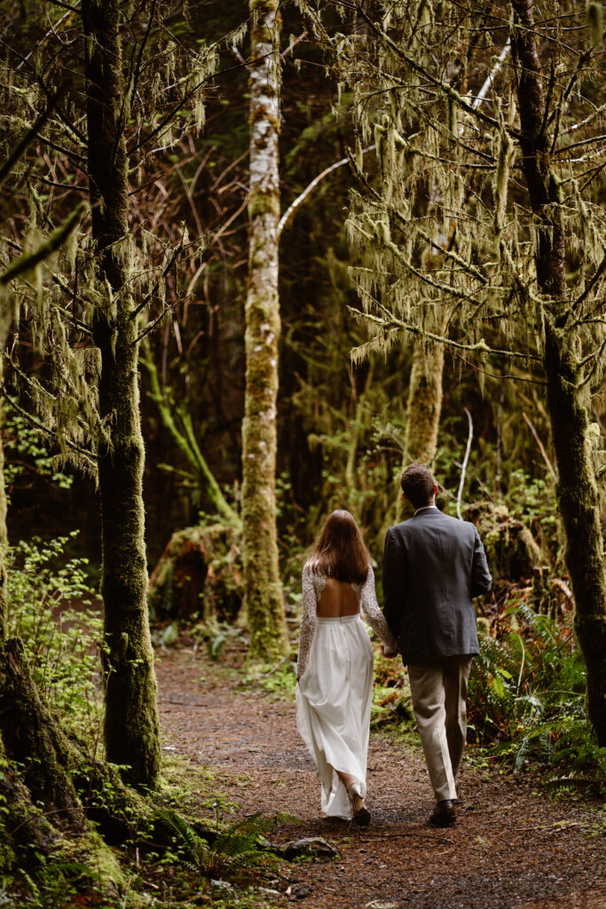 a bride and groom hold hands and walk down a trail during their olympic peninsula elopement