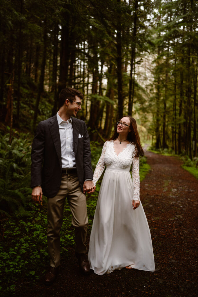 a bride and groom hold hands and explore a trail during their olympic peninsula elopement