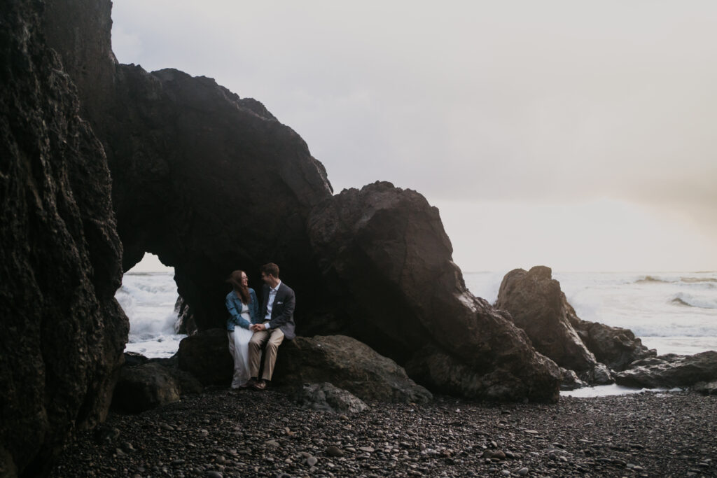 a couple sits on an arched rock during their ruby beach elopement