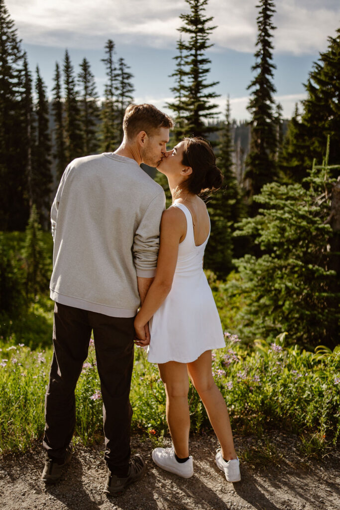 a couple kisses while holding hands on trail the the mount rainier paradise meadows