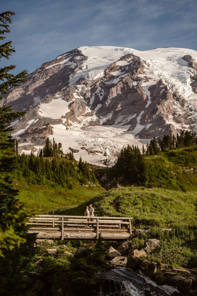 a couple stands on a bridge with mt. rainier in the background