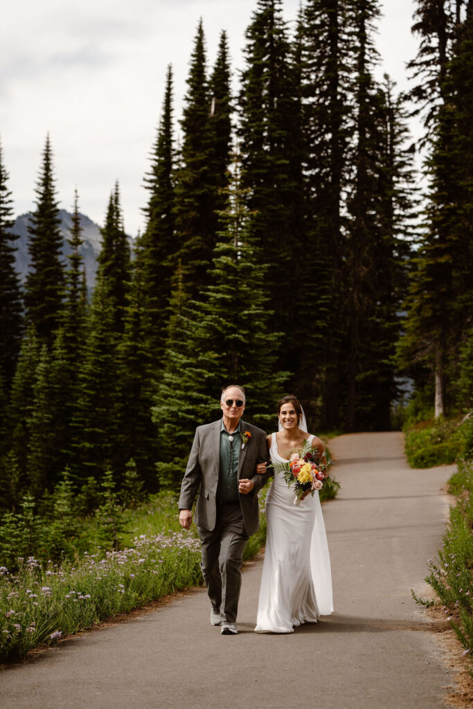 a bride is walked down the trail by her father during a mt rainier micro wedding