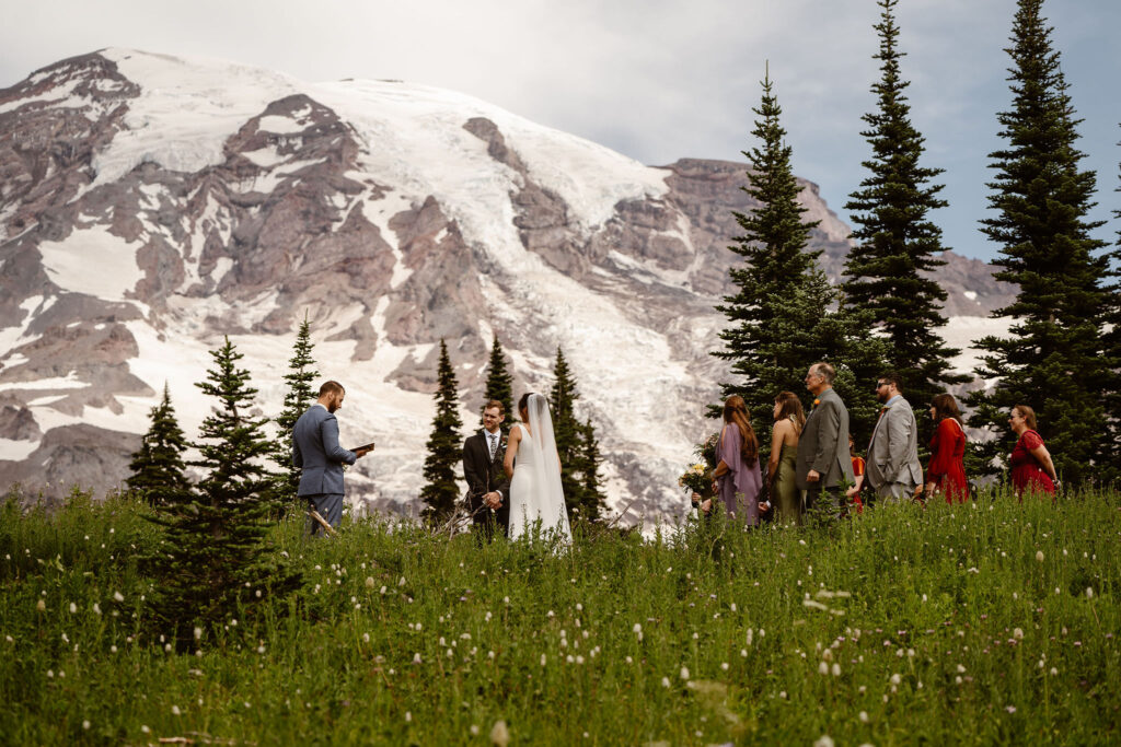 a bride, groom, officiant, and their families stand for a Mount Rainier elopement ceremony surrounded by wildflowers