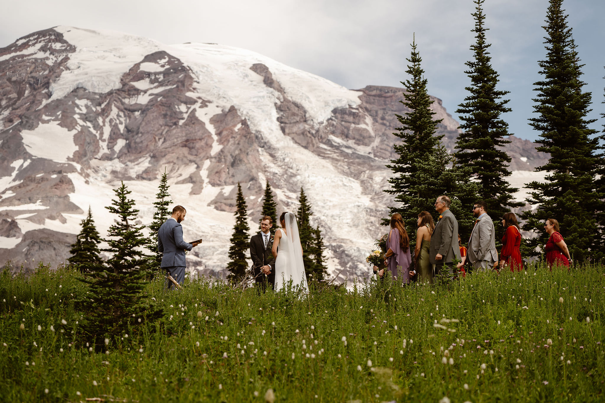 a bride, groom, officiant, and their families stand for a Mount Rainier elopement ceremony surrounded by wildflowers