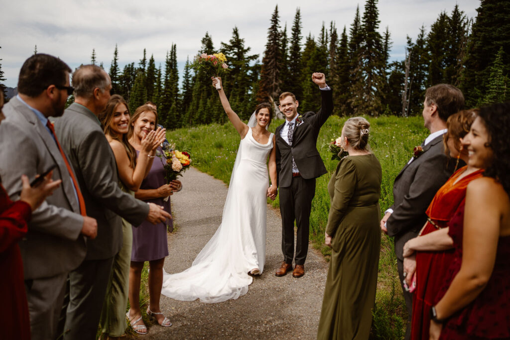 a bride and groom raise their hands in celebration during their mt rainier micro wedding