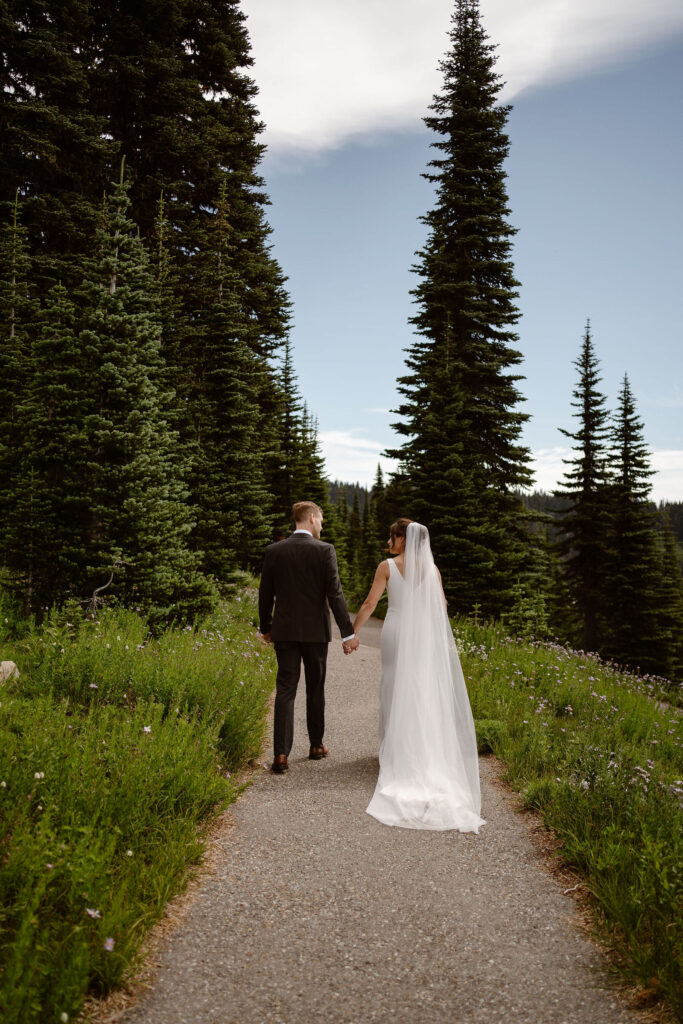 a bride and groom hold hands and walk down the trail during their mt rainier micro wedding