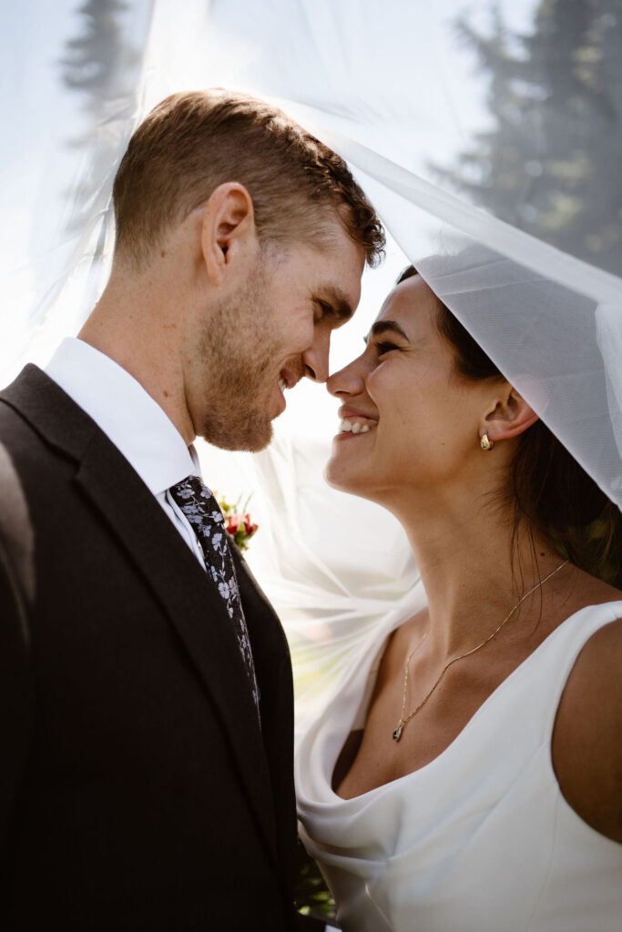 a bride and groom nuzzle noses underneath a veil during their mount rainier micro wedding