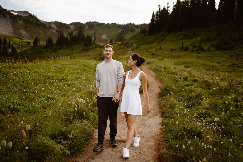 a couple holds hands and walks down a trail at mount rainier