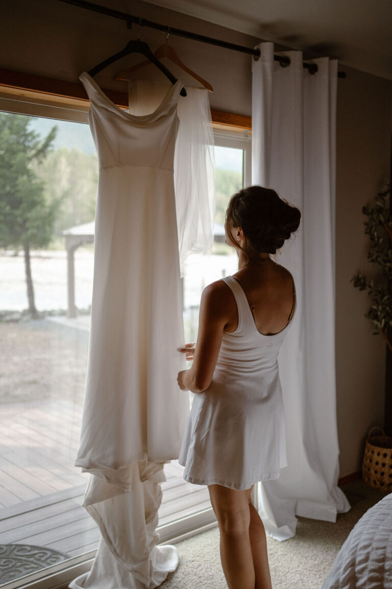 a bride examines her dress handing in front of a window while getting ready for her mt rainier micro wedding reception dinner