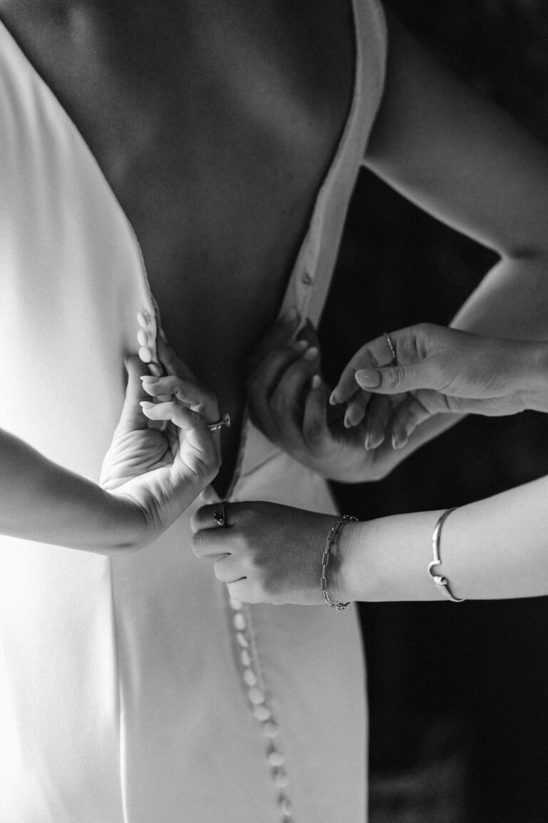 a bride's sister helps button the bride's dress while getting ready for a mount rainier micro wedding reception dinner