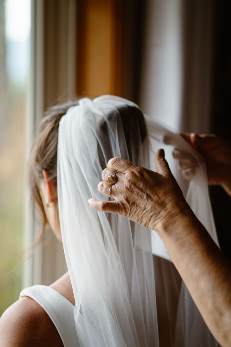 the bride's mom helps adjust her veil while getting ready for