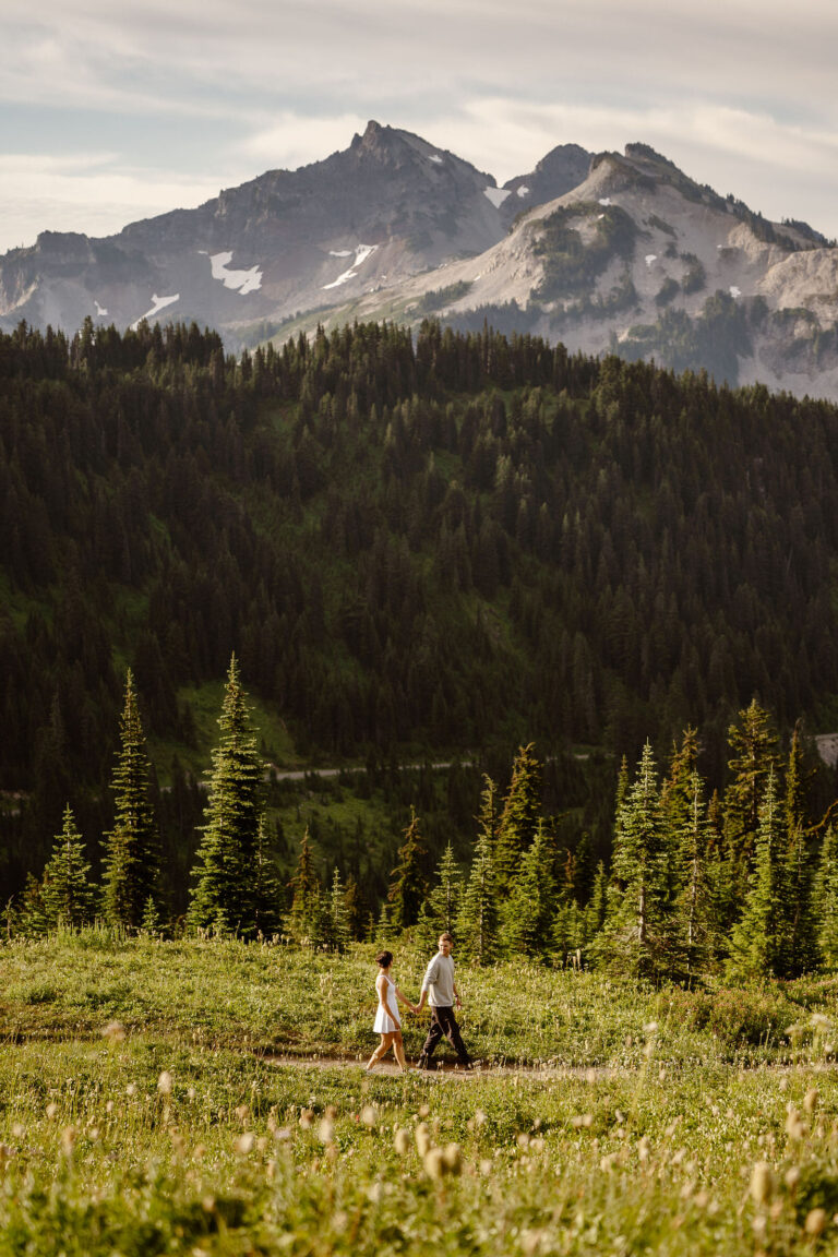a couple holds hands and walks down a trail through the paradise meadows at mount rainier