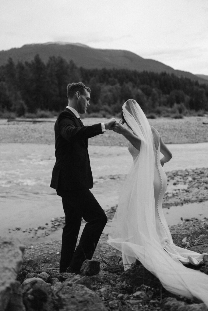 a groom helps a bride walk down a hill during their mount rainier micro wedding