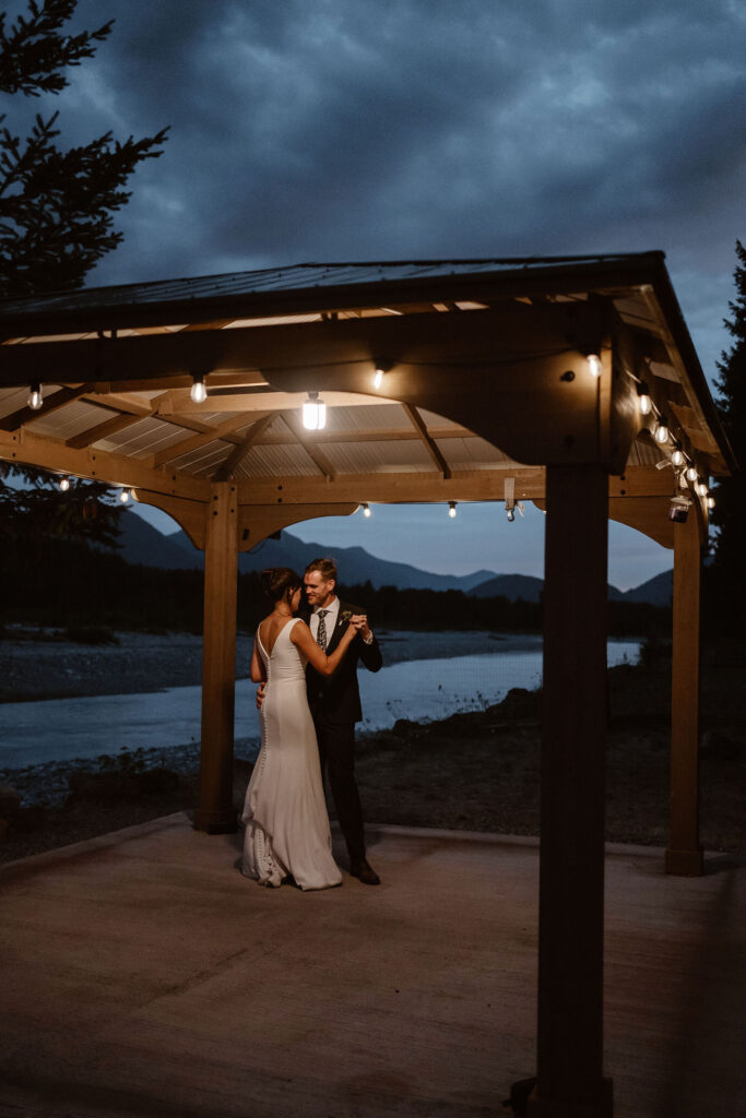 a bride and groom share a first dance at blue hour under a gazebo with string lights
