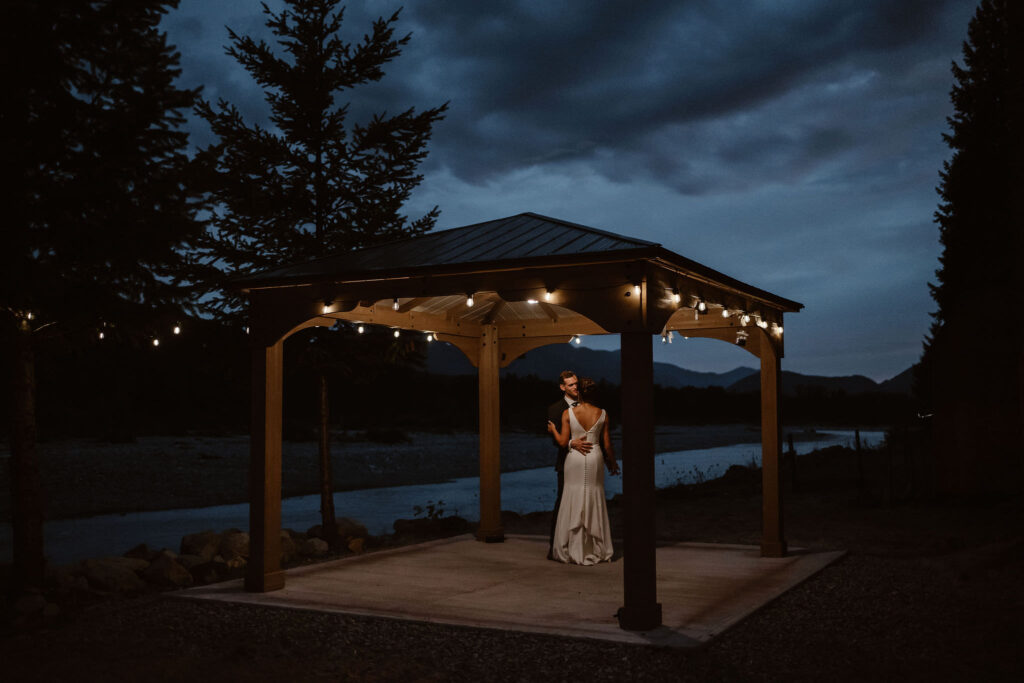 a couple shares their first dance under a gazebo with string lights at blue hour